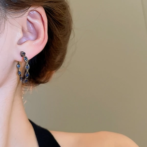 Detailed view of dark grey hollow chain earrings with deep blue zircons on model