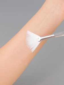Macro shot of Fan Mask Brush applying liquid to skin showing soft white bristles