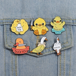 Close-up of six funny enamel duck pins with 'Duck You' slogans on a blue denim jacket