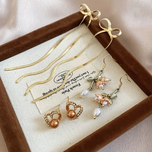 Detailed close-up of bow tassel, vintage flower pearl and heart earring set on display