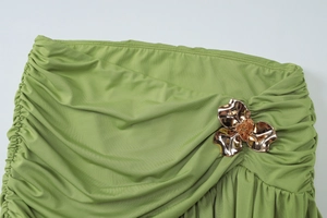 Macro detail of grass green pleated fabric featuring a rose gold metal floral ornament
