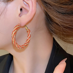 Detailed side view of twisted spiral hoop earrings with sparkling texture and gold-red finish