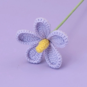 Close-up of hand-knitted purple flower with yellow center and green stem decoration