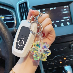 Detail of a rainbow crystal flower keychain hanging on a white car key fob in luxury car interior
