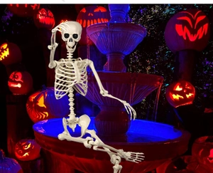 Detailed full body Halloween skeleton prop sitting by a blue lighted fountain decoration