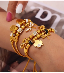 Detail of gold layered charm bracelet with dragonfly, clover, and infinity pendants