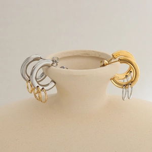 Interlocked metallic C-shaped hoop earrings in gold and silver finish on ceramic vase