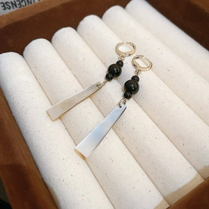 Macro detail of long drop earrings featuring black beads and mother of pearl pendants