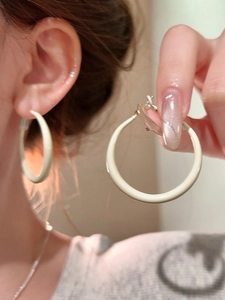 Detail of cream-colored large hoop earrings showing the smooth matte finish on a model