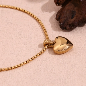 Macro detail of 18K gold-plated heart pendant with elegant box chain on textured background