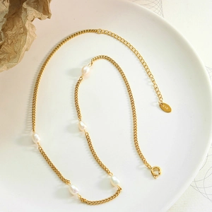 Flat lay of a gold flat chain necklace with natural freshwater pearls on a white plate