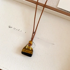 Close-up of heart-shaped tiger eye stone pendant with wooden bead on brown suede cord