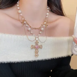 Layered gold cross necklace with pearls and pink heart gemstone on fashion model
