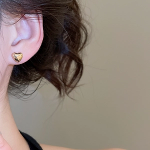 Close-up of a model wearing a shiny golden heart-shaped stud earring for a minimalist look
