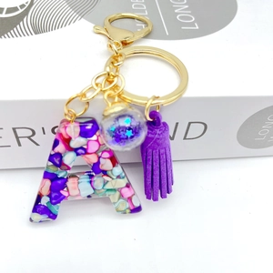Close-up of resin letter A keychain with purple tassel and colorful stone inlay