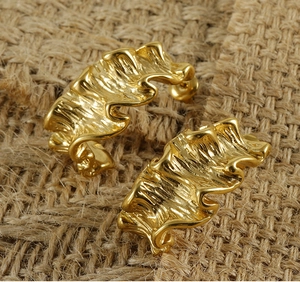Macro shot of 18K gold-plated titanium earrings with wavy sculpted texture on burlap