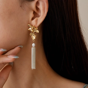 Boucles d'oreilles fleur dorée avec perle blanche et pompons chaînés sur mannequin