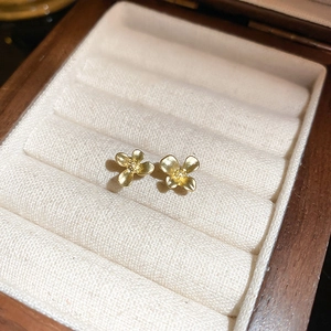 Boucles d'oreilles fleurs dorées élégantes avec texture mate sur boîte à bijoux