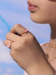 Detail showing two gold butterfly rings with pink enamel on fingers against blue sky background