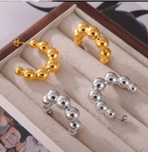 Detailed view of gold and silver beaded C-shaped stud earrings in a wooden jewelry box
