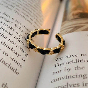 Dettaglio dell'anello in pelle intrecciata placcato oro con zirconi su un libro