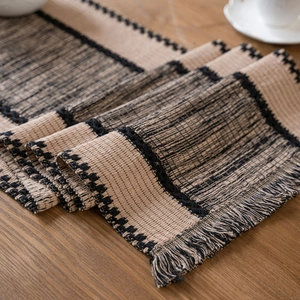 Beige and black striped woven table runner with decorative tassels on wooden table