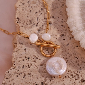 Detail of baroque pearl pendant with golden T-bar toggle clasp on a textured stone surface