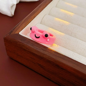 Close-up of pink frog cartoon resin ring resting on a beige velvet jewelry box tray