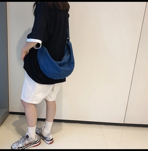 Deep blue denim crescent hobo bag shown in use on the back of a model in a casual style