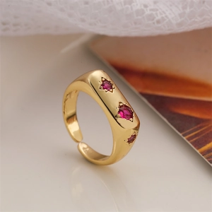 Détail macro de la bague ajustable dorée avec trois zircons rouges sertis en étoiles