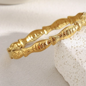 Macro view of gold plated fish pattern cuff bracelet resting on a textured white stone