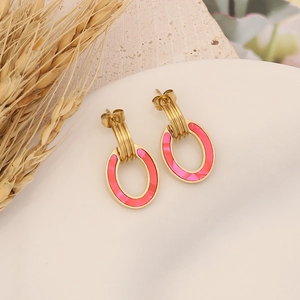 Macro view of gold geometric hoop earrings with magenta oval pendants on a white plate