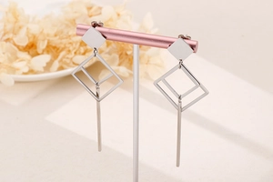 Detail view of silver geometric diamond earrings on a pink display stand with soft lighting