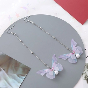 Détail de boucles d'oreilles ailes de papillon avec perles et chaîne argentée sur plateau