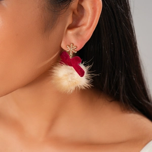 Detail of earring featuring golden snowflake, red velvet bow, and beige fur pompom