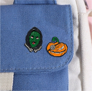 Detail of creative Halloween enamel pins featuring a green witch and orange pumpkin on a bag