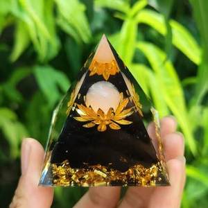 Pyramide d'orgonite avec pierres noires et motif lotus tenue à la main