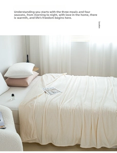 Detailed view of cream-colored waffle knit blanket draped over a cozy bedroom bed