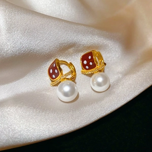 Macro detail of 18K gold plated pearl earrings with red enamel on silk background