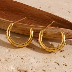 Close-up of C-shaped 18K gold-plated earrings with pavé zircons on a stone pedestal