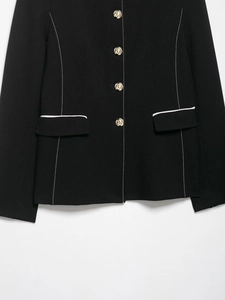 Detailed macro view of black blazer with contrast white stitching and gold buttons