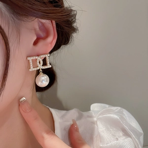 Close-up of elegant gold letter earring with a large white pearl and sparkling crystals