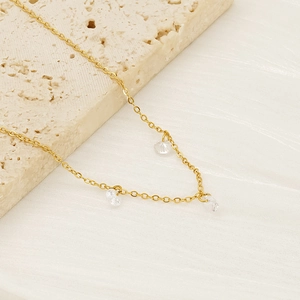 Minimalist gold necklace with three clear zircon pendants on a beige stone surface