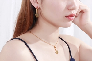 Close-up of gold heart MOM necklace and earrings set worn by a model in bright light