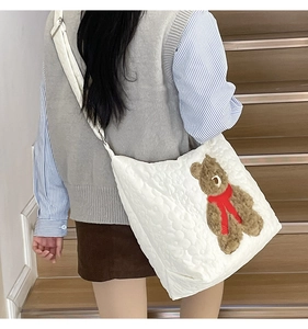 Quilted white crossbody tote bag with a brown teddy bear applique shown on a staircase