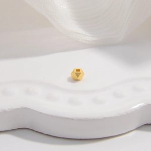 Macro shot of faceted gold S925 silver cylinder bead on a white ceramic tray