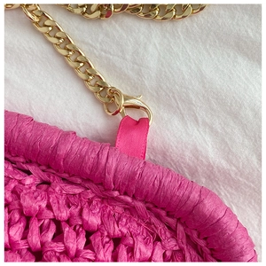 Macro shot of hot pink straw woven bag edge with gold metal chain strap detail