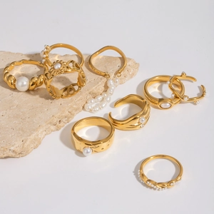 Set of 8 gold stainless steel rings with pearls displayed on natural stone props