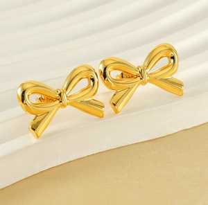 Detailed macro view of 18K gold-plated stainless steel bow earrings on a wavy pedestal