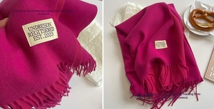 Macro view of rose red cashmere scarf with dense long tassels and woven brand label detail